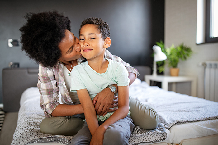 A smiling mother and son resting on a bed.